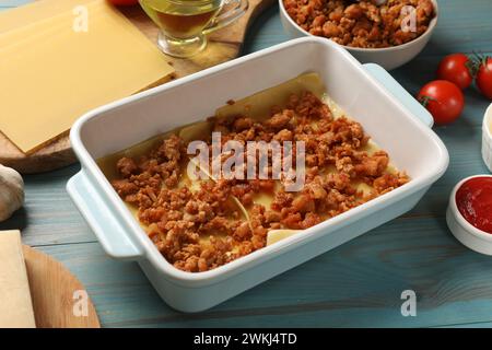 Lasagne kochen. Nudellaken und Hackfleisch in Backblech auf hellblauem Holztisch, Nahaufnahme Stockfoto