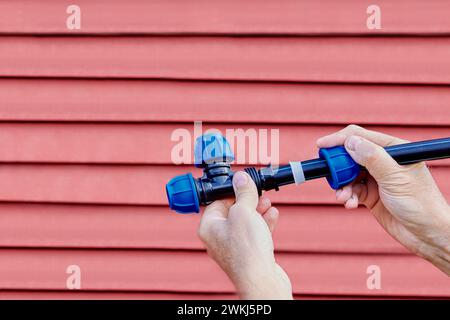 Installation eines externen Rohrleitungssystems mit dreifacher Druckverschraubung, Klempner eingefügtes Rohr im T-Stück, roter Hintergrund, Nahaufnahme. Stockfoto