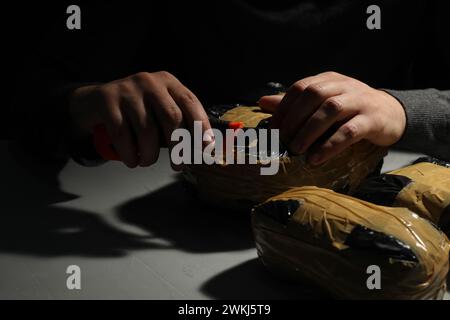 Schmuggel und Drogenhandel. Mann, der ein Paket mit Betäubungsmitteln öffnet, mit einem Koffer in der Dunkelheit, Nahaufnahme Stockfoto