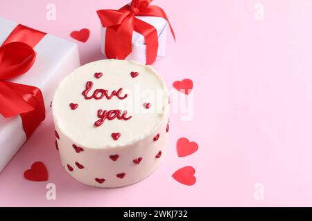 Bento Kuchen mit Text Love You, Geschenkboxen und Papierherzen auf rosa Tisch, Platz für Text. St. Valentinstag-Überraschung Stockfoto