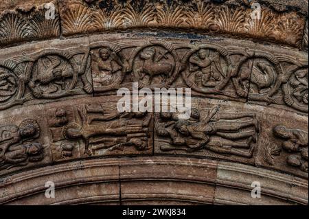 Kopfüber Kreuzigung des Apostels Petrus (unten Mitte links). Eine der Szenen aus dem Leben von St. Peter und St. Paul in Relief in einem Archivolt über dem Eingang zur Basilika des Klosters Santa Maria de Ripoll in der Provinz Girona, Katalonien, Spanien. Der Eingang wurde Mitte der 1100er Jahre im lombardischen romanischen Stil gestaltet. Der Überlieferung nach wurde der hl. Peter, der 64 n. Chr. in Rom während der Herrschaft von Kaiser Nero starb, kopfüber gekreuzigt, weil er glaubte, er sei unwürdig, wie Christus zu sterben. Über dem Petersdom befindet sich das Lamm Gottes und andere christliche Symbole. Stockfoto