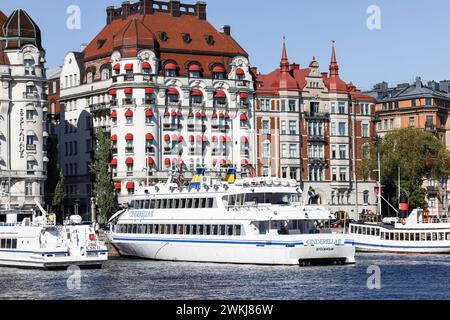 Historische Gebäude im Jugendstilhotel Strandvagen 7 Diplomat (rotes Baldachin) hinter Booten und Fähren in Nybroviken, Ostermalm, Stockholm Stockfoto