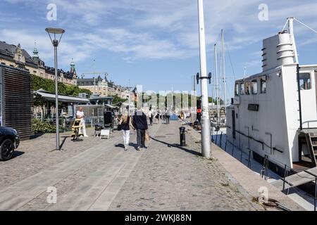 Auf der historischen Strandvagen-Uferpromenade spazieren die Menschen an Cafés, Bars und Booten im Ladugårdslandsviken-See, Ostermalm, Stockholm Stockfoto