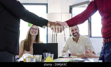 Eine Gruppe von Einzelpersonen, die an einem Tisch sitzen und sich als Begrüßung oder Vereinbarung mit dem Handschlag befassen. Verschiedene Geschäftskollegen. Stockfoto