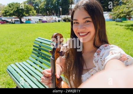 Selfie-Porträt einer jungen lateinischen Buskerin, die glücklich lächelt, während sie auf der Straße eine Kamera ansieht, die ihre Geige hält, und auf der plaza in Buenos Aires Ar steht Stockfoto