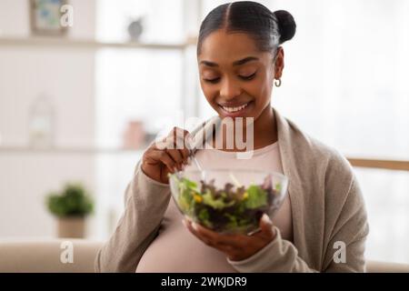 Porträt einer glücklichen jungen schwangeren Frau, die zu Hause Salat isst Stockfoto