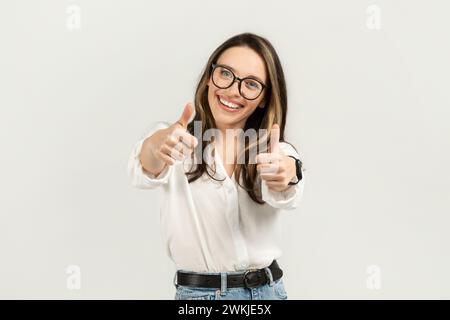 Begeisterte junge Frau mit brünetten Haaren und Brille, die zwei Daumen hoch hält Stockfoto