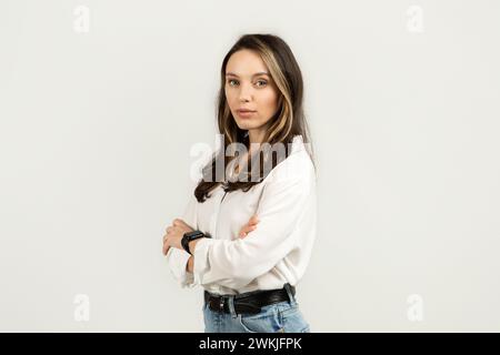 Stern aussehende junge Frau mit überkreuzten Armen in weißer Bluse und Jeans Stockfoto