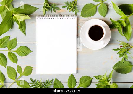 Frühlingskomposition mit offenem leerem Notizblock, Tasse schwarzen Kaffee, grünen Blättern auf Holztisch. Kaffeetasse am Morgen. Stockfoto