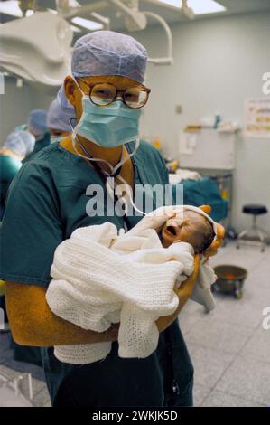 NHS 1980s Doktor Phil Hammond hält ein Baby, das gerade durch Kaiserschnitt im Royal United Hospital Bath geboren wurde. Somerset, England 1988 1980er Jahre, UK HOMER SYKES Stockfoto