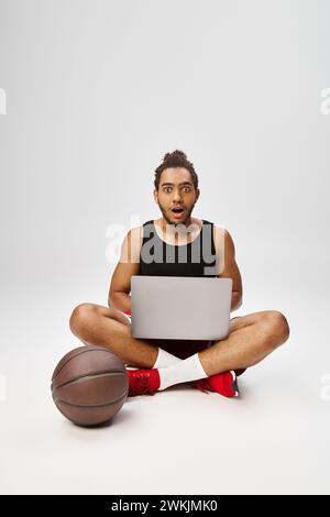 Schockierter afroamerikanischer Mann in Sportbekleidung, der mit Laptop sitzt und in die Kamera schaut, Online-Wetten Stockfoto