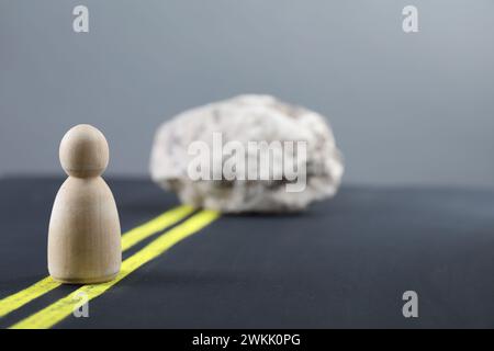 Überwindung von Barrieren für Entwicklung und Erfolg. Holzfigur Bewegung blockiert durch Stein auf der Straße, Platz für Text Stockfoto