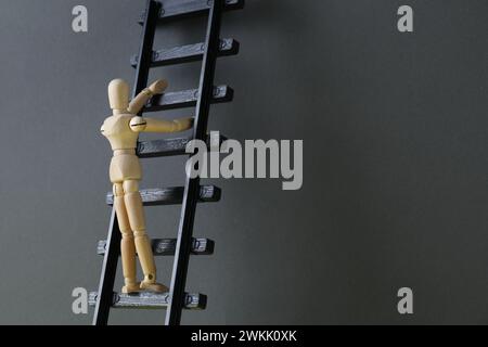 Überwindung von Barrieren für Entwicklung und Erfolg. Eine menschliche Holzfigur, die die Spielzeugleiter in der Nähe einer grauen Wand hochklettert, Platz für Text Stockfoto