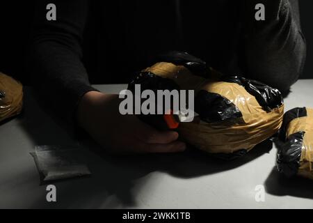 Schmuggel und Drogenhandel. Mann, der ein Paket mit Betäubungsmitteln öffnet, mit einem Koffer in der Dunkelheit, Nahaufnahme Stockfoto