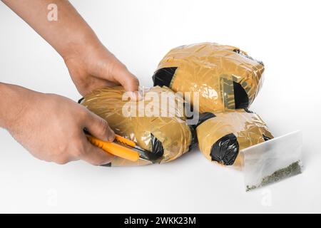 Schmuggel und Drogenhandel. Mann, der ein Paket mit Betäubungsmitteln mit einem Koffer auf weißem Hintergrund öffnet, Großaufnahme Stockfoto