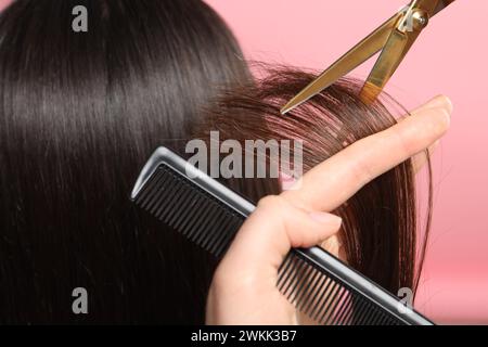 Friseur schneidet die Haare des Kunden mit einer Schere auf rosa Hintergrund, Großaufnahme Stockfoto