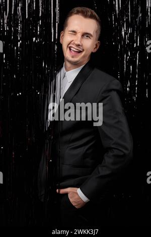 Hübscher Mann in schwarzer Jacke, der auf die Kamera blickt, mit glücklichem Ausdruck auf Glitzerhintergrund. Stockfoto