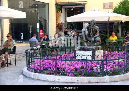 Menschen essen und trinken am Bronzestatue Monument für Kostas Georgakis in der Altstadt von Korfu, Griechenland, EU. Stockfoto