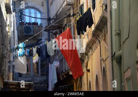 Waschen hängt an der Kleiderschnur draußen in der engen Straße zwischen Gebäuden und über Geschäften in der Altstadt von Korfu, Griechenland, EU. Stockfoto