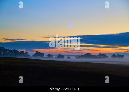 Nebliger Sonnenaufgang mit Windturbinen in ländlicher Landschaft Stockfoto