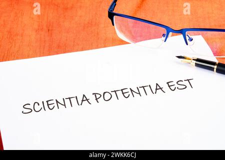 Der Satz Scientia Potentia Est (Wissen ist Macht) steht in lateinischer Sprache auf einem weißen Stück Papier auf dem Tisch neben der Brille Stockfoto