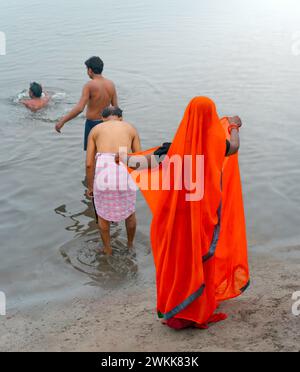 Eine Frau in traditionellem Saree und drei Männer nehmen ein rituelles Bad, während die Dämmerung über dem heiligen Yamuna-Fluss in Vrindavan, Großbritannien, bricht. Stockfoto