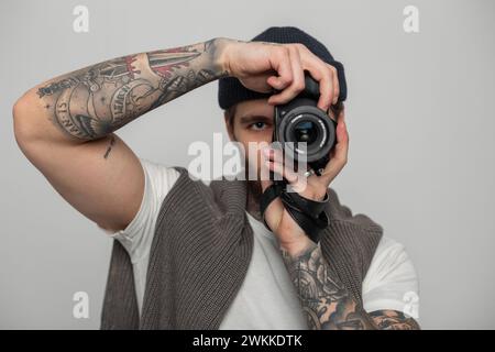Hübscher, kreativer Hipster-Fotograf mit Strickmütze und Pullover, der im Studio Fotos macht und in die Kamera schaut. Stockfoto