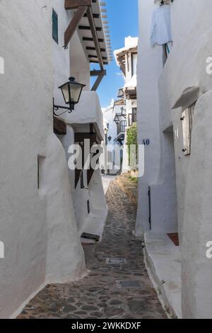 Binibeca Vell, Spanien - 24. Januar 2024: Enge Gasse führt durch ein Labyrinth von weiß getünchten Gebäuden im Dorfzentrum von Binibeca Vell Stockfoto