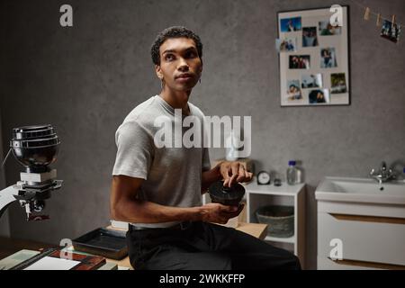 Hübscher junger afroamerikanischer Fotograf, der einen Filmkanisterdeckel in einer Dunkelkammer sichert Stockfoto