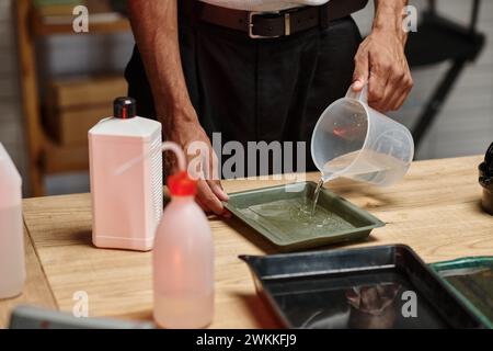 Abgeschnittener dunkelhäutiger Mann, der Filmentwicklungslösung in Dunkelkammer vorbereitet, analoge Fotografie Stockfoto