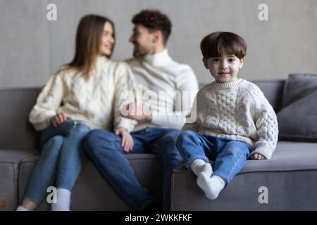 Lachende glückliche junge Familie posiert zusammen im Wohnzimmer mit einem entzückenden Jungen mit fehlenden Vorderzähnen, flankiert von seinem attraktiven lächelnden p Stockfoto