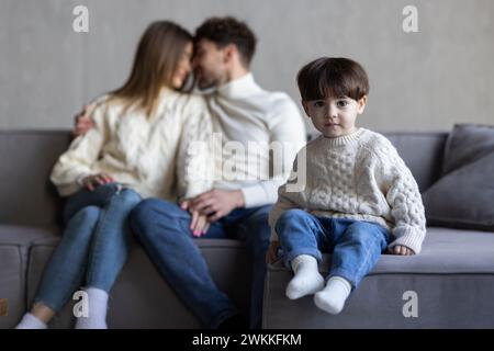 Lachende glückliche junge Familie posiert zusammen im Wohnzimmer mit einem entzückenden Jungen mit fehlenden Vorderzähnen, flankiert von seinem attraktiven lächelnden p Stockfoto