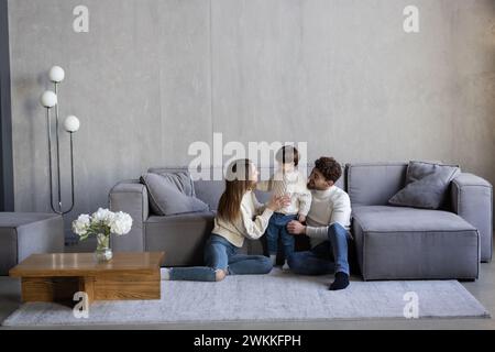 Lachende glückliche junge Familie posiert zusammen im Wohnzimmer mit einem entzückenden Jungen mit fehlenden Vorderzähnen, flankiert von seinem attraktiven lächelnden p Stockfoto