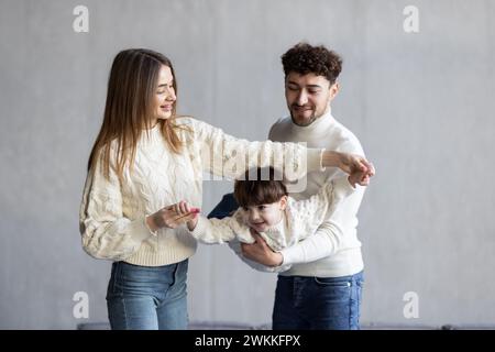 Ganzkörpervater und Mutter lächeln und heben gemischten Sohn nahe der Couch Stockfoto