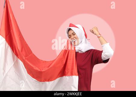 Junge asiatische Frau, die glückliche Unabhängigkeit der republik indonesien in rot-weißem Satin mit lächelndem Ausdruck auf rosa Hintergrund feiert, ausgeschnitten Stockfoto
