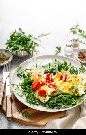 Spiegelei, Omelette mit Zwiebeln, Tomaten und frischem Rucolasalat Stockfoto