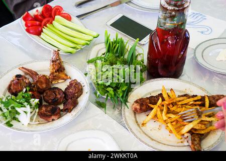 Verschiedene Shish Kebabs, Gemüse, Salat mit frischen Tomaten und Gurken auf dem Tisch, nationale, östliche Gerichte Stockfoto