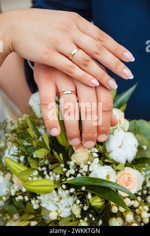 Eheringe an den Händen des Brautpaares die Braut und der Bräutigam halten ihre Hände an einem Blumenstrauß, Hochzeitsstrauß in Nahaufnahme, Idee Stockfoto