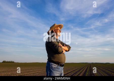 Senior Farmer, der bei Sonnenuntergang auf dem Maisfeld steht. Stockfoto