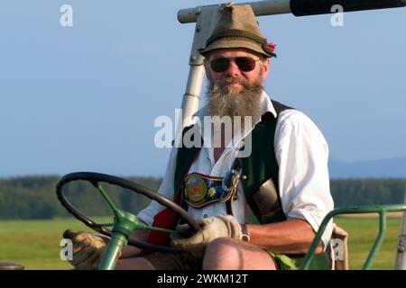 Traditionell gekleideter Bauer in Lederhosen und Tiroler Hut auf einem Traktor, Dietramszell, Bayern, Deutschland Stockfoto