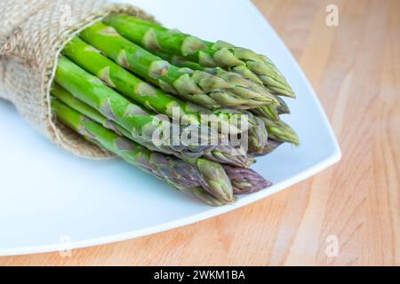 Bund frischer Spargel auf Holztisch und weißem Teller, gesundes Essen Stockfoto
