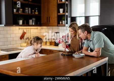 Eine herzerwärmende Szene entfaltet sich, während eine Familie einen köstlichen Schokoladenkuchen zusammen in der Wärme ihrer sonnendurchfluteten Küche genießt und Lächeln und cr teilt Stockfoto