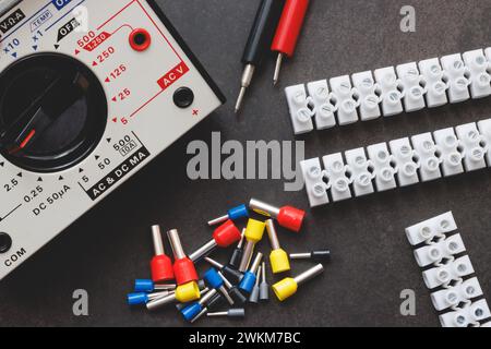 Schließen Sie mehrere Aderendhülsen und Klemmenblock mit Draht und Multimeter auf einem schwarzen Tisch Stockfoto