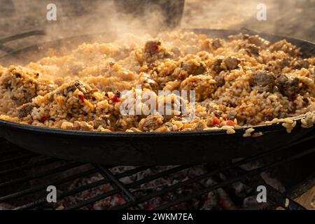 Eine große Paella, die über dem Feuer kocht, mit einem rauchigen Hintergrund, Street Food Stockfoto