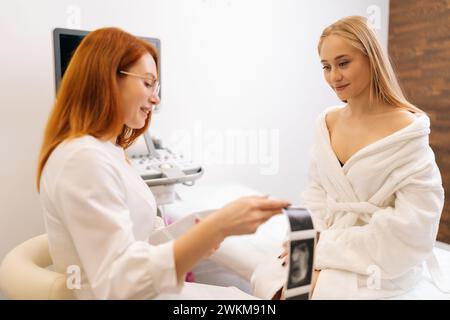 Professionelle Ärztin überprüft Ergebnisse der Ultraschalluntersuchung und erklärt der jungen Patientin Magier. Arzt erklärt Ergebnisse von Stockfoto