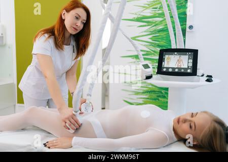 Entspannte Patientin in weißem Anzug mit Anti-Cellulite-LPG-Massage. Professionelle Frau Masseurin, die Massage mit LPG-Apparatemaschine für Stockfoto