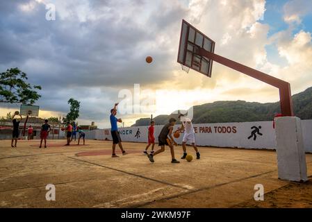 Vinales, Kuba - 6. Februar 2023: Lokale Jungen stellen sich bei Sonnenuntergang in einem dynamischen Outdoor-Basketballspiel vor. Berge im Hintergrund Stockfoto