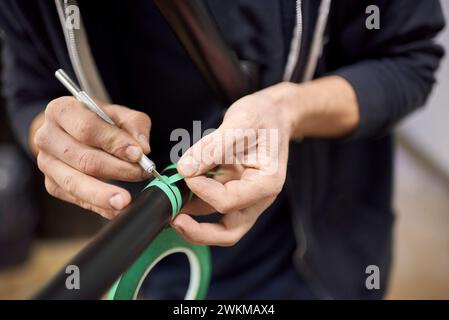 Unbekannte Person, die einen Fahrradrahmen mit Skalpell und Abdeckband für eine individuelle Bemalung in seiner Fahrradwerkstatt vorbereitet. Stockfoto