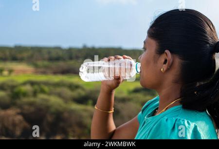 Eine junge Wanderer macht eine Pause, um sich mit einem kühlen Getränk aus ihrer wiederverwendbaren Wasserflasche zu rehydrieren Stockfoto