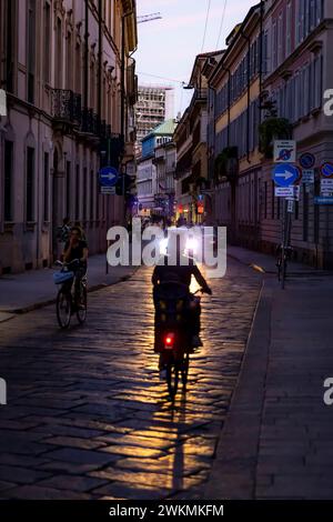 Eine Frau fährt mit dem Fahrrad, wenn die Nacht über Mailand hereinbricht. Stockfoto